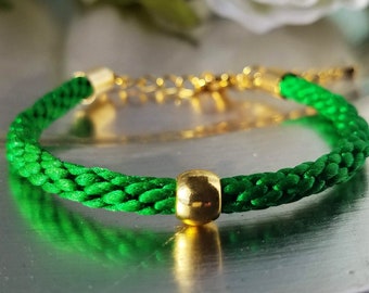 Grönt armband med klövermotiv för St. Patrick's Day: Handvävt i grön satintråd med en rund guldpläterad accentpärla och justerbart spänne.