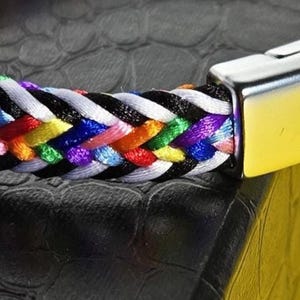 May include: A braided bracelet with a silver clasp. The bracelet is made of multiple colored threads, including red, orange, yellow, green, blue, purple, pink, and white.