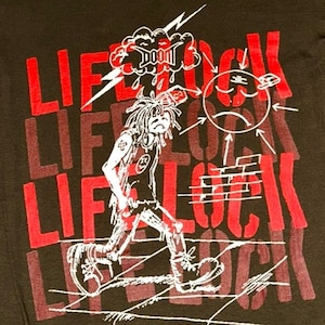 May include: A green t-shirt with a white and red graphic print. The graphic features a cartoon character walking with a lightning bolt and the word "LIFELOCK" repeated multiple times.