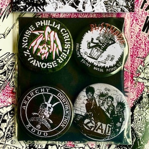 Op de afbeelding: Vier ronde zwart-witte punkrockband-knoppen met grafische ontwerpen. De knoppen tonen de tekst "Z-Noise Phila. Cluster", "Filthy Noise Attack EP", "Anarchy Destruction" en "GAI".