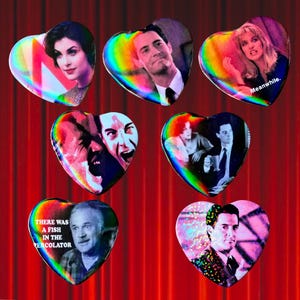 May include: A selection of heart-shaped badges with images of characters from the TV series Twin Peaks. Each badge has a holographic rainbow border. One badge reads "Meanwhile.", and another reads "THERE WAS A FISH IN THE PERCOLATOR."