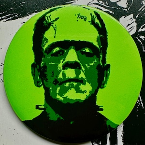 May include: A green and black illustration of Frankenstein's monster on a round, green background.