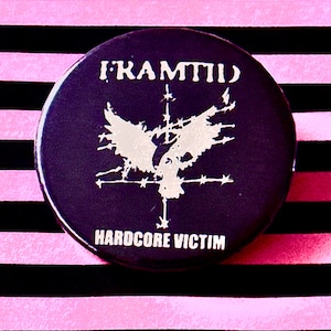 Peut inclure: Un bouton noir avec un graphique d'oiseau blanc et le texte "KRAMTII" et "HARDCORE VICTIM".