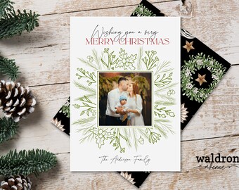 May include: A white Christmas card with a green floral border and a photo of a family of three. The text "Wishing you a very Merry Christmas" is written in red and black. The text "The Anderson Family" is written at the bottom of the card.