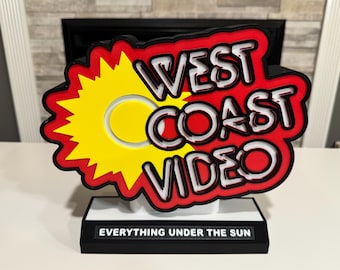 以下が含まれることがあります： 「West Coast Video」という文字と黄色の太陽の光が描かれた赤、白、黒の看板。看板には黒い台座に「Everything Under The Sun」という文字も書かれている。
