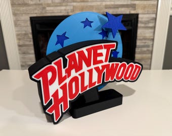 以下が含まれることがあります： プラネットハリウッドのロゴの3Dプリントモデル。ロゴは黒のアウトラインで赤と白。ロゴは、後ろに星のある青と白の地球儀のある黒いベースの上にあります。