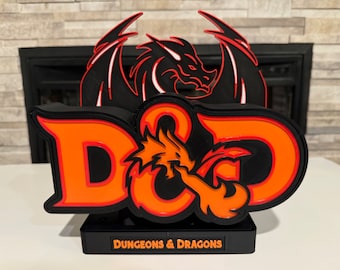 May include: A black and orange Dungeons & Dragons logo with a dragon design. The logo is on a black base with the words "Dungeons & Dragons" printed on the front.