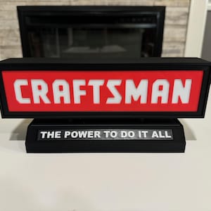 May include: A black and red sign with the word "CRAFTSMAN" in white letters. The sign also has the text "THE POWER TO DO IT ALL" in white letters.