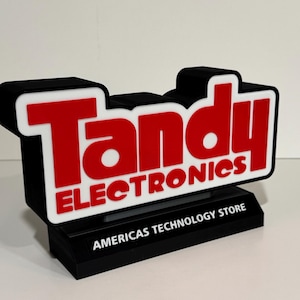 May include: A black and white Tandy Electronics sign with red lettering. The sign reads "Tandy Electronics" and "AMERICAS TECHNOLOGY STORE". The sign is a 3D printed model.
