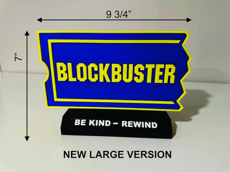 以下が含まれることがあります： 黒色の台座に「Be Kind - Rewind」の文字が書かれた青と黄色のブロックバスターの看板。看板の幅は24.7cm、高さは17.8cm。新しい大型バージョンです。