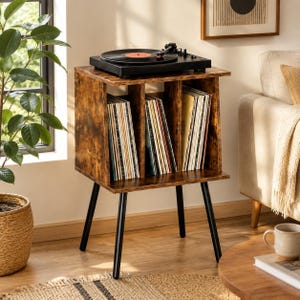 May include: A brown wood-grain record player stand with three vertical storage compartments filled with vinyl records. The stand features a flat top surface holding a black turntable and is supported by four thin, black, angled metal legs.