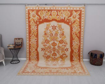 May include: A vintage rug with a floral pattern in shades of orange, yellow, and white. The rug has a central medallion with a floral design and a border with a repeating floral motif.