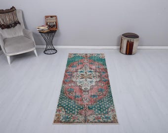 May include: A rectangular, vintage-style rug with a central floral medallion in shades of pink, cream, and teal. The rug features a distressed look, with a teal border and intricate patterns. The rug is placed on a light-colored wooden floor.
