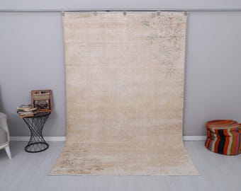 Può includere: Un grande tappeto vintage color crema con un delicato motivo floreale. Il tappeto è appeso a una parete e ha un aspetto usurato e rovinato.
