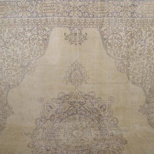 Puede incluir: Una alfombra beige grande con un intrincado patr&oacute;n floral descolorido en tonos grises y topo. La alfombra presenta un dise&ntilde;o de medall&oacute;n central y bordes ornamentados, creando una est&eacute;tica vintage. La alfombra est&aacute; doblada, mostrando su tama&ntilde;o.