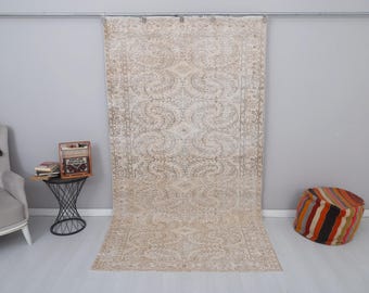 May include: A large, off-white rug with a floral pattern. The rug has a light brown border and a central medallion with a more intricate design. The rug is hanging on a wall.