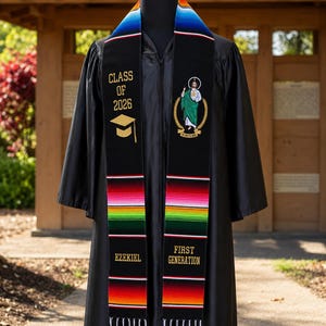 May include: A black graduation stole featuring a multi-colored striped pattern at the neck and ends with white fringe. The left side displays "CLASS OF 2026" and a mortarboard icon. The right side features a religious figure and "FIRST GENERATION".