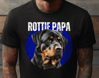 May include: A black t-shirt with a blue circle graphic featuring a Rottweiler dog. The text "Rottie Papa" is printed in white above the graphic.