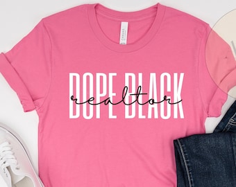 May include: Pink t-shirt with the text "Dope Black realtor" in white lettering.