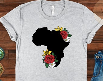 Puede incluir: Una camiseta gris con una silueta negra del continente africano adornada con flores rojas, amarillas y blancas.