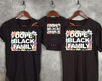 May include: Three black t-shirts with a floral design and the text "Dope Black Family" in white. The shirts are on hangers against a gray background.