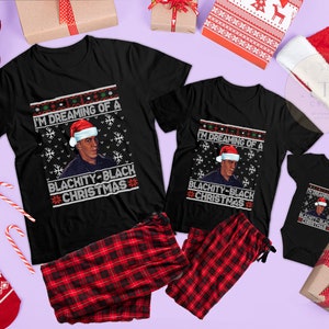 Op de afbeelding: Een set van drie zwarte T-shirts met een kerstthema met een afbeelding van een persoon met een kerstmanmuts en de tekst "I'm dreaming of a Blachity-Black Christmas".