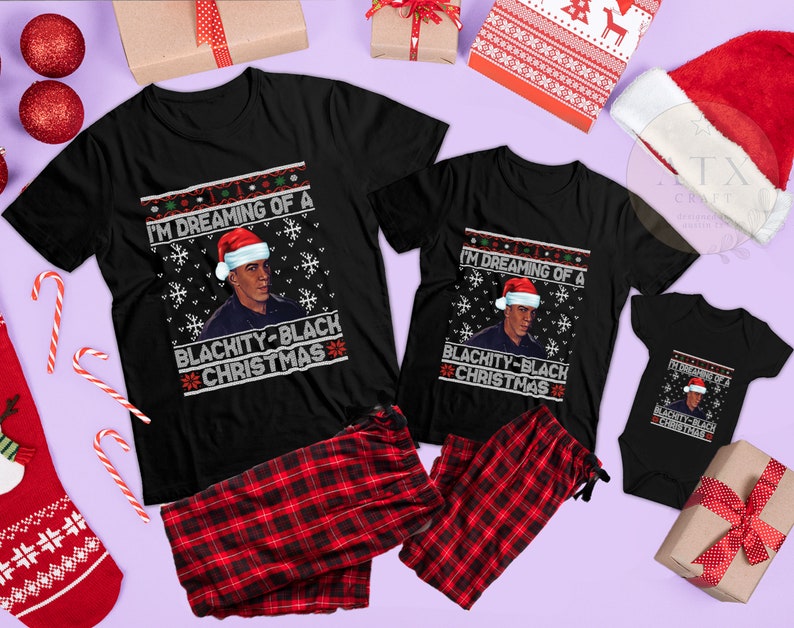 Op de afbeelding: Een set van drie zwarte T-shirts met een kerstthema met een afbeelding van een persoon met een kerstmanmuts en de tekst "I'm dreaming of a Blachity-Black Christmas".