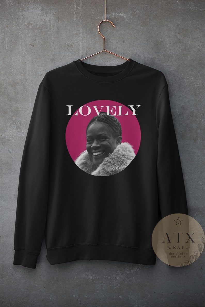 May include: Black sweatshirt with a pink circle featuring a woman smiling. The text "LOVELY" is above the circle. The sweatshirt has a white star and the text "ATX CRAFT designed in austin, tx" on a brown tag.