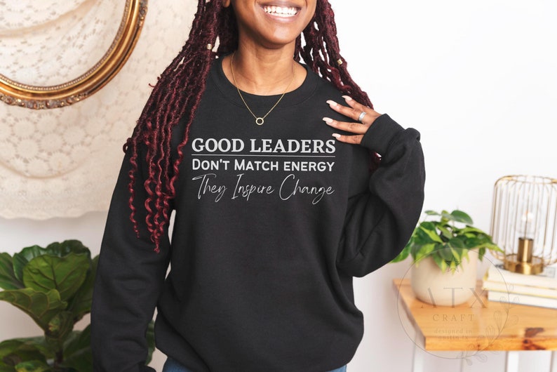 May include: Black sweatshirt with white text that reads "Good Leaders Don't Match Energy They Inspire Change".