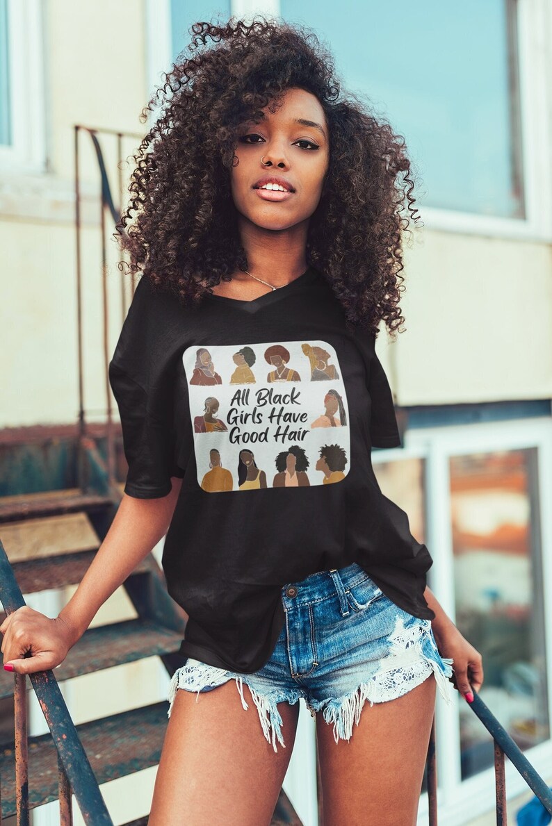 Peut inclure: Un t-shirt noir avec un graphique carr&eacute; blanc repr&eacute;sentant un collage de femmes noires avec diff&eacute;rentes coiffures. Le texte "All Black Girls Have Good Hair" est imprim&eacute; en blanc sur le graphique.