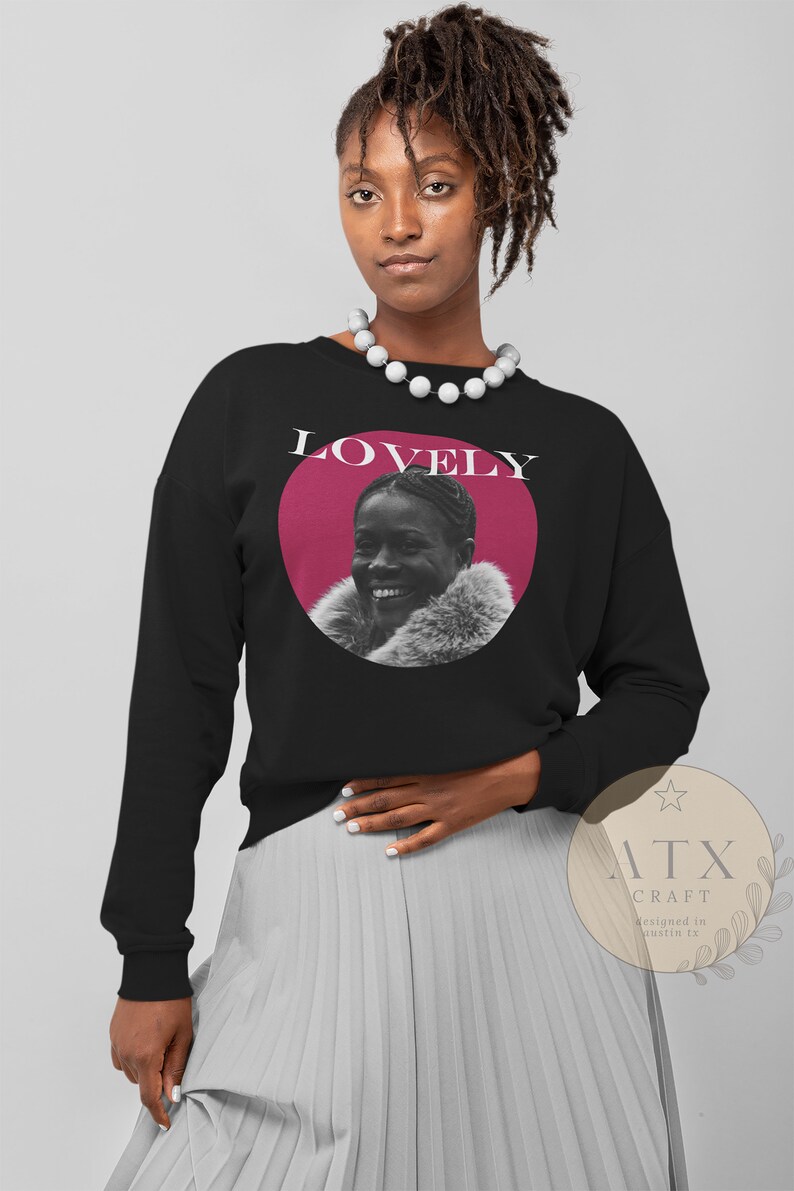 May include: Black sweatshirt with a pink circle and a black and white photo of a woman smiling. The text "LOVELY" is printed in white above the circle.