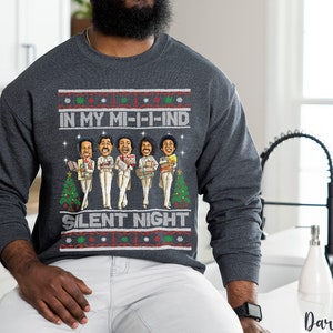 May include: A dark heather grey sweatshirt with a Christmas-themed design featuring a group of cartoon characters holding gifts. The text on the sweatshirt reads "In My Mi-i-ind Silent Night".