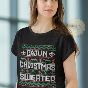 May include: A black t-shirt with a festive design featuring the text "Cajun Christmas Sweater" in white. The design includes red and green snowflakes, fleur-de-lis, alligators, and crawfish.