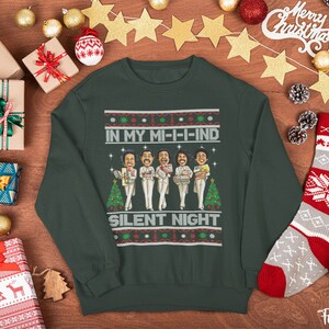 May include: A forest green Christmas sweater with a festive design featuring a group of cartoon figures singing "In My Mi-I-I-Ind Silent Night".