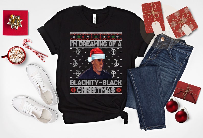 Op de afbeelding: Zwarte kersttrui met een zwart-wit sneeuwvlokkenpatroon. De trui heeft een portret van een man met een kerstmanmuts en de tekst "I'm Dreaming of a Blackity-Black Christmas".