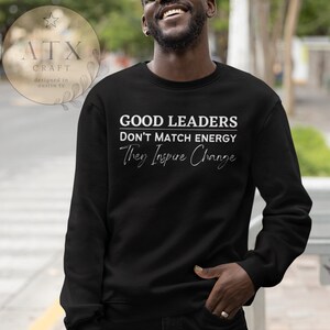May include: Black sweatshirt with white text that reads "Good Leaders Don't Match Energy They Inspire Change".