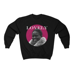 May include: Black sweatshirt with a pink circle and the word "LOVELY" in white text. Inside the circle is a black and white photo of a woman smiling.