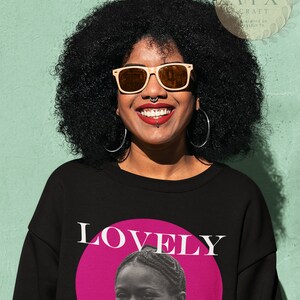 May include: A black sweatshirt with a pink circle and the word "LOVELY" in white text. Inside the circle is a black and white photo of a woman with a fur collar smiling.