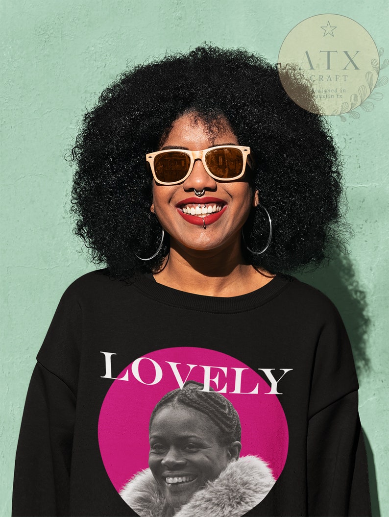 May include: A black sweatshirt with a pink circle and the word "LOVELY" in white text. Inside the circle is a black and white photo of a woman with a fur collar smiling.