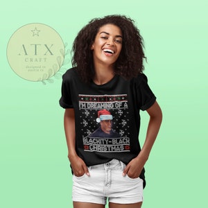 Op de afbeelding: Zwart-witte kersttrui met een rode kerstmanmuts op het hoofd van een persoon. De trui heeft de tekst "I'm dreaming of a Blackity-Black Christmas".