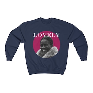 May include: Navy blue sweatshirt with a pink circle and the word "LOVELY" in white text. Inside the circle is a black and white photo of a woman with a fur collar.