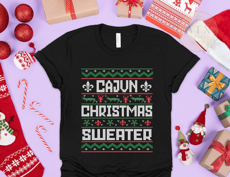 May include: Black t-shirt with a green, red, and white Christmas sweater design. The design features a fleur-de-lis, alligators, and crawfish. The text on the shirt reads "Cajun Christmas Sweater".