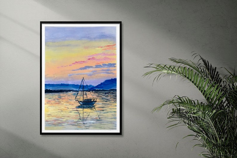 May include: A framed watercolour painting depicting a sailboat on tranquil water at sunset. The sky transitions from yellow to pink and blue, with the boat's reflection visible. The artwork is in a black frame.