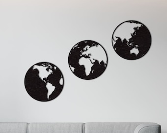 May include: Three black wooden wall decor pieces shaped like the Earth with a white outline of the continents. The decor is displayed on a white wall above a gray couch.