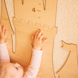 May include: A child reaches up to a wooden castle-shaped growth chart with a number "4" marked on it. The chart is mounted on a wall.