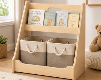 May include: A light-colored wooden bookshelf featuring a top shelf holding four children's books titled Guess How Much I Love You, You Are My Happy, Little Owl's Day, and I Love You Always, with two beige and tan fabric storage bins below.