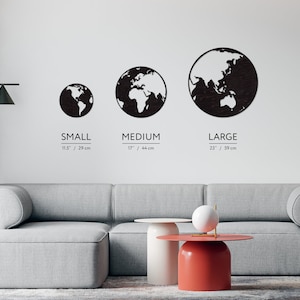 May include: Three black wooden world map wall decor pieces in different sizes: small (11.5 inches / 29 cm), medium (17 inches / 44 cm), and large (23 inches / 59 cm). The pieces are hanging on a white wall above a gray couch.
