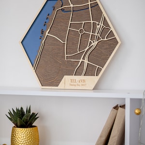 May include: A wooden map of Tel Aviv, Israel, with a blue water feature and brown streets. The map is in a hexagonal shape and has the text "Tel Aviv Dating Day 2017" on the bottom.