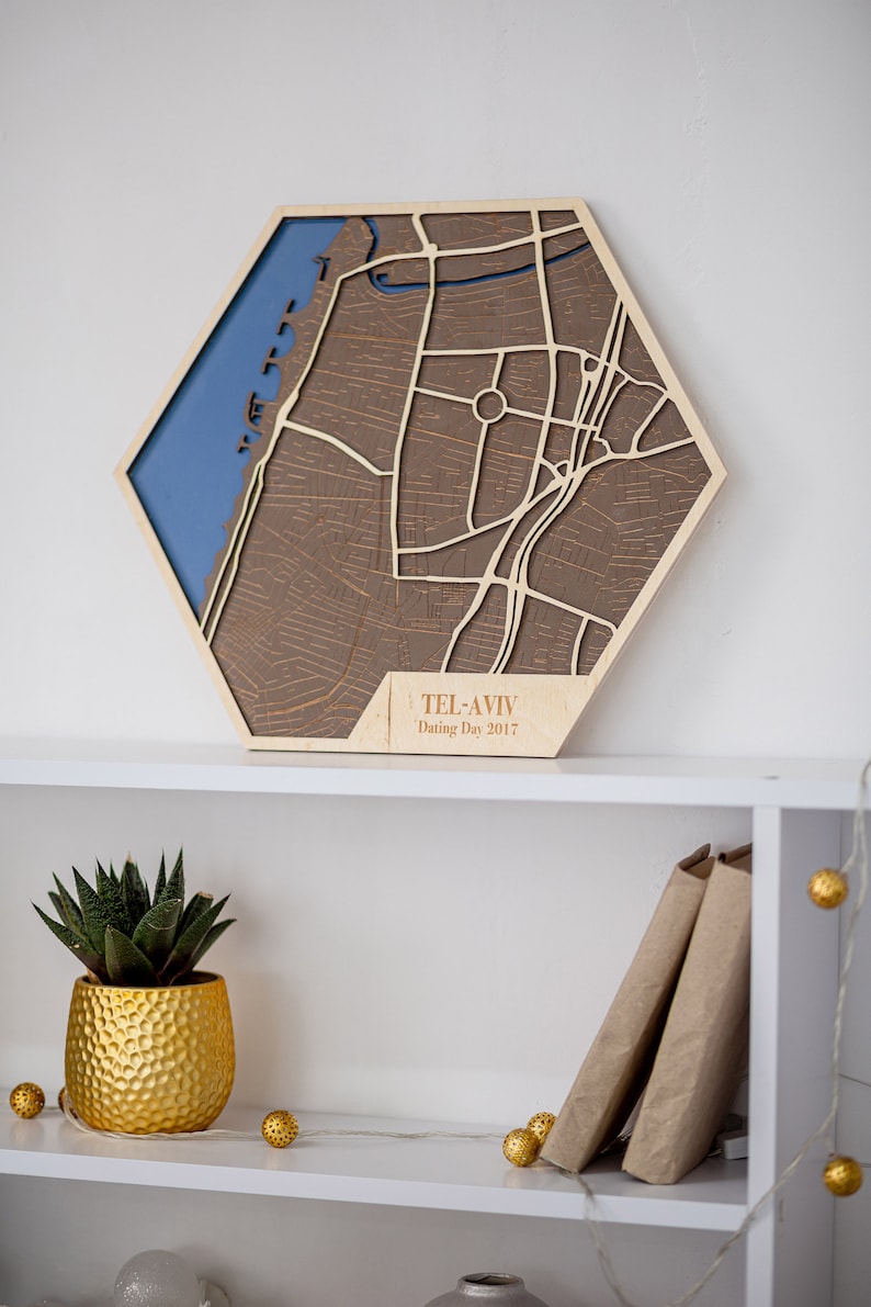 May include: A wooden map of Tel Aviv, Israel, with a blue water feature and brown streets. The map is in a hexagonal shape and has the text "Tel Aviv Dating Day 2017" on the bottom.