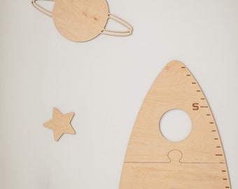May include: Wooden rocket ship growth chart with a cutout for a child's head and a ruler on the side. The chart is decorated with a planet, a star, and a smaller star.